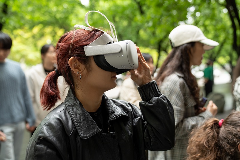 야외 테라스 공간에서 한 관객이 VR 헤드셋을 착용하고 공연 콘텐츠를 감상하고 있다.