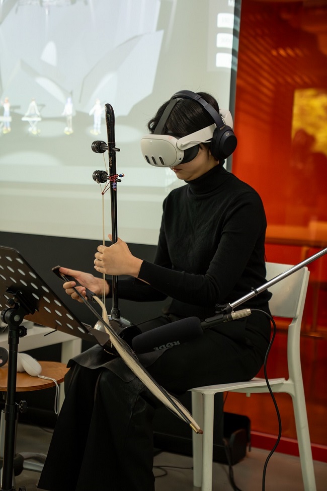 연주자가 VR 헤드셋과 헤드폰을 착용한 채 한국 전통 악기인 해금을 연주하고 있다.